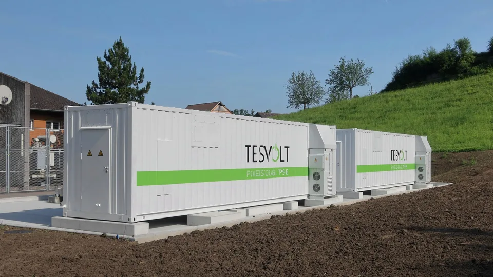 スイス・ラインエックの草地の脇に並ぶ白いコンテナ型Tesvolt蓄電池システム2基
