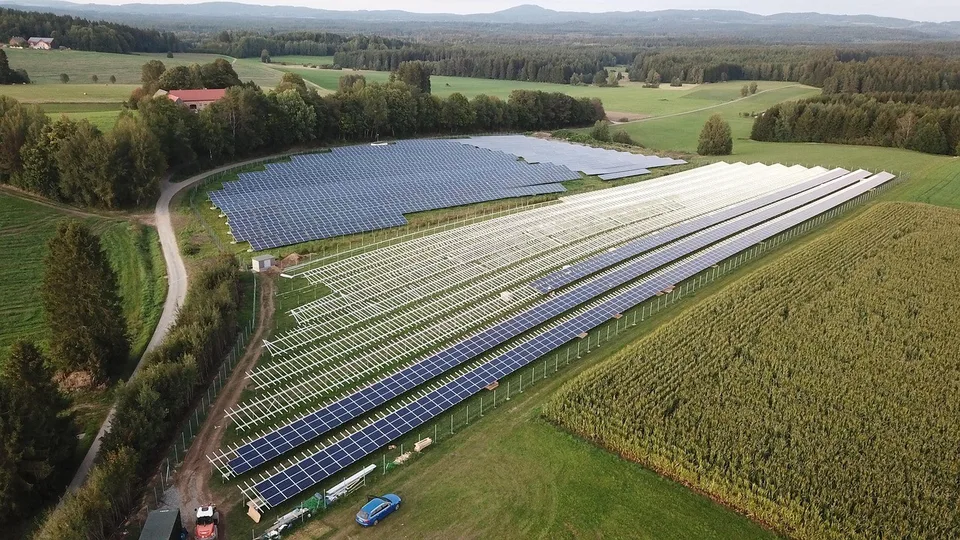 Aerial view of a solar farm in rural Bavaria, Germany, with rows of panels between green fields and woodland
